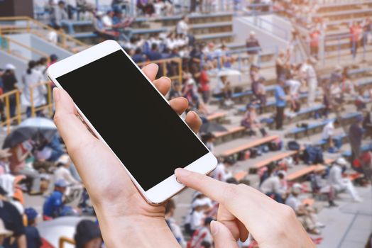 Woman hold smart phone and touch button by hand with blank screen for advertisement, Stadium and audiences background ,Technology and Sport concept