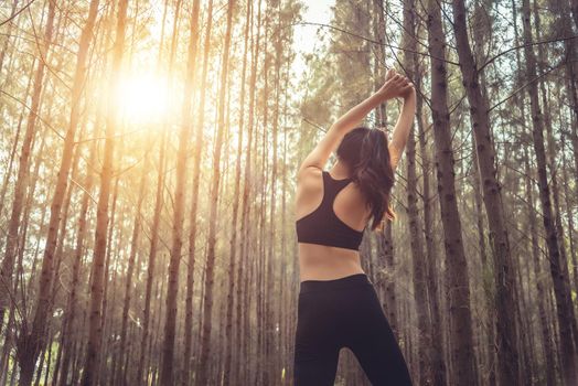 Beautiful slim female runner do stretching arms and warm up to running in peaceful forest in morning. Workout and exercise concept. Healthy in nature concept. Pine woods in autumn seasonal theme.