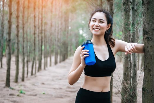 Asian beauty woman drinking water in forest. Sport and Healthy concept. Jogging and Running concept. Relax and take a break theme. Outdoors activity theme.