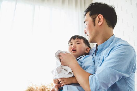 Asian Japanese father consoling his crying son and wiping tears in bedroom at his home white curtain background. People lifestyle health. Medical and Health concept. Negative emotion theme.