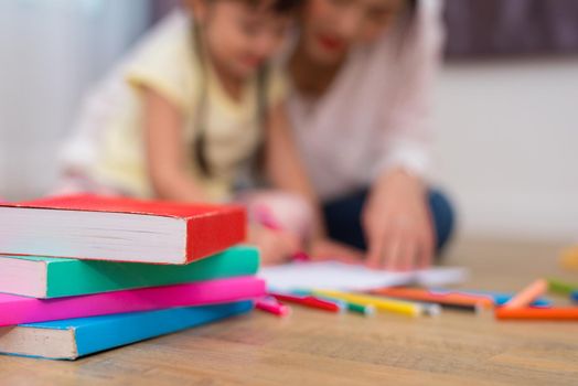 Close up of books and crayon color on floor with mom and kids background. Back to school and Art education learning concept. Children and teacher theme.