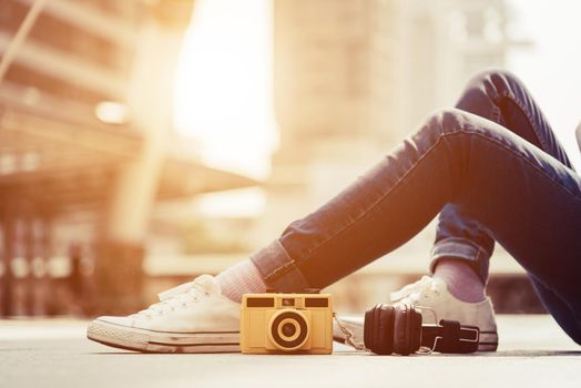 Woman legs wearing jeans and resting and relax in middle of city. Vintage camera and Stereo headphones elements Fashion and Modern technology concept. Happy life of teenager theme. Lifestyle in urban