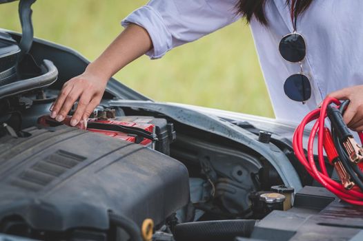 Closeup of woman hand holding battery cable copper wire for repairing broken car by connect battery with red and black line to electric terminal by herself. Car maintenance and transportation concept