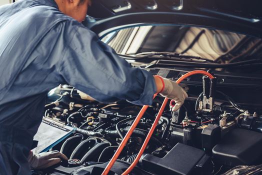 Car mechanic holding battery electricity trough cables jumper and checking to maintenance vehicle by customer claim order in auto repair shop garage. Repair service. People occupation and business job
