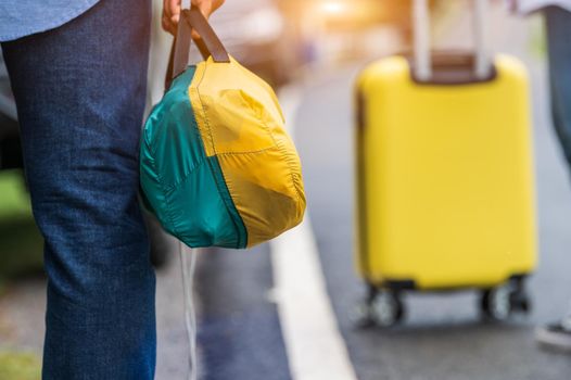 Closeup of tourist legs walking along road with bag during travel in countryside. People lifestyles and vacation concept. Man holding and backpacking for long holiday trip with mountain background