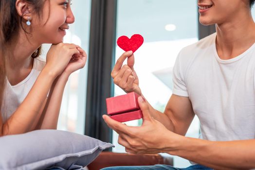 Man holding gift box for surprise girlfriend at their home. Woman waiting for Valentines gift form boyfriend. Happy Birthday party anniversary concept. People couple lifestyles and family life theme