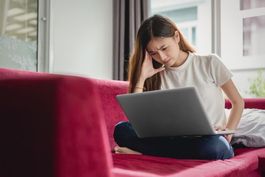 Exhausted businesswoman having a headache while using laptop on red sofa, Business worry and Stress concept, Online shopping and marketing concept.