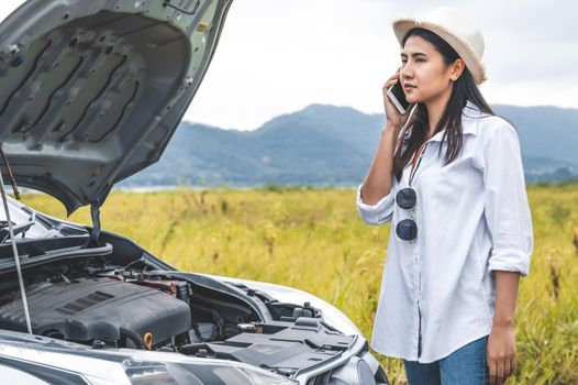 Asian woman calling car mechanic service for repairing breakdown broken car by mobile phone during driving to destination. Car maintenance and transportation concept. People travel and landscape theme
