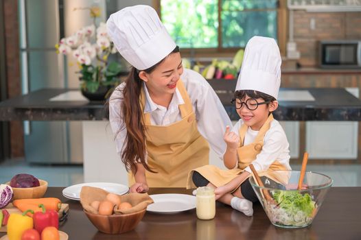 Happy beautiful Asian woman and cute little boy with eyeglasses prepare to cooking in kitchen at home. People and Family concept. Homemade food and ingredients concept. Two Thai people lifestyles