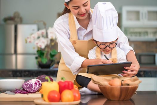 Asian beauty mother and cute little boy prepare online shopping and listing ingredient for cooking in kitchen at home with tablet. People lifestyles and Family. Homemade food and ingredient concept