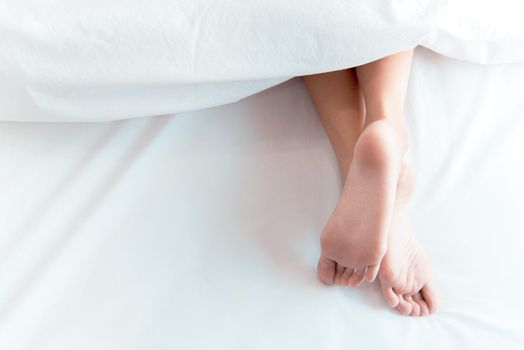 Woman feet on the bed under white blanket. Sleeping and relax concept. Vacation and Holiday theme