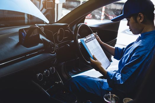 Mechanic holding clipboard and checking inside car to maintenance vehicle by customer claim order in auto repair shop garage. Repair service. People occupation and business job. Automobile technician