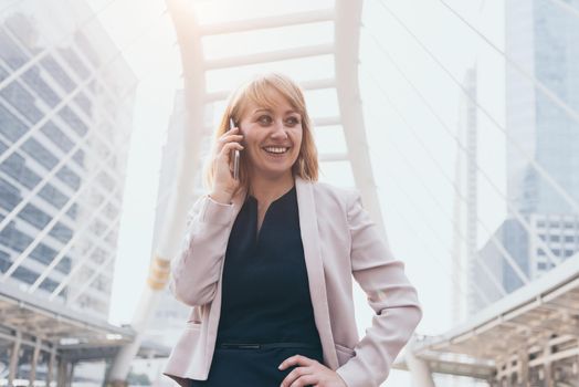 Happy businesswoman using smart phone to communicate and talk to business agreement in urban city background. People lifestyles and technology concept. Outdoor working and social distancing concept
