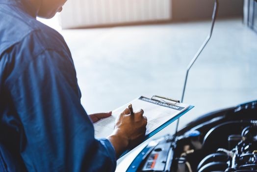 Car mechanic holding clipboard and checking to maintenance vehicle by customer claim order in auto repair shop garage. Engine repair service. People occupation and business job. Automobile technician