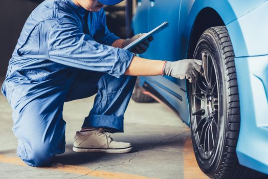 Asian car mechanic technician holding clipboard and checking to maintenance vehicle by customer claim order in auto repair shop garage. Wheel tire repair service. People occupation and business job