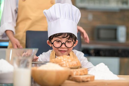 Portrait cute little Asian happy boy interested in cooking funny in home kitchen. People lifestyles and Family. Homemade food and ingredients concept. Baking Christmas cake and cookies. Smiling child