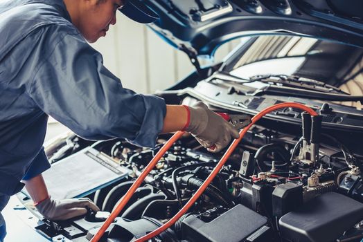 Car mechanic holding battery electricity trough cables jumper and checking to maintenance vehicle by customer claim order in auto repair shop garage. Repair service. People occupation and business job