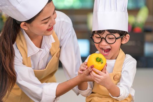 Portrait cute little Asian happy boy chef interested in cooking with mother funny in home kitchen. People lifestyles and Family. Homemade food and ingredient concept. Vegetable salad making