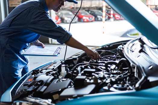 Car mechanic holding clipboard and checking to maintenance vehicle by customer claim order in auto repair shop garage. Engine repair service. People occupation and business job. Automobile technician