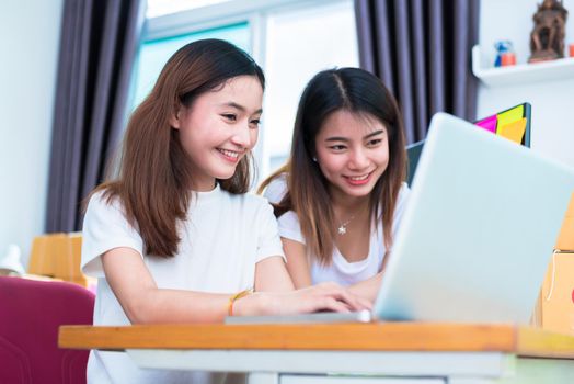 Two young freelancer Asian girl businesswomen private working at home office with laptop or computer with notebook on desk. packaging delivery online shopping and marketing service to customer