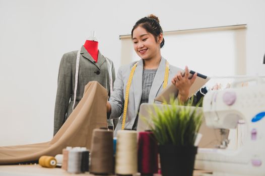 Fashion designer stylist in business owner workshop with tablet and customer contact list. Tailor and sew concept. Portrait of happy casual trendy fashion businesswoman in studio. Job and occupation