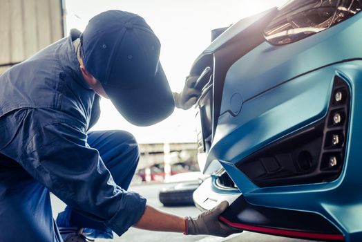 Mechanics installing front skirt at auto repair shop garage. Transportation and Business concept. Automobile technician maintenance vehicle by customer claim order. Car salon accessories decoration
