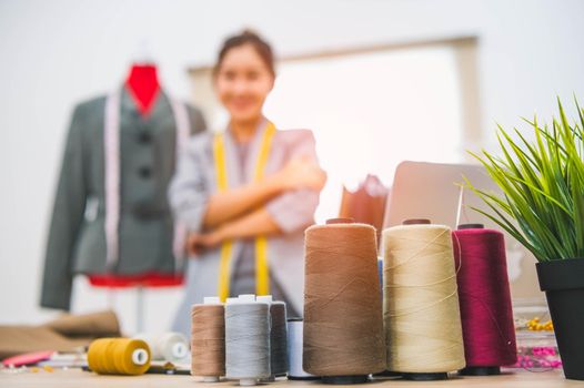 Closeup of color thread with blurry happy female tailor and sewing clothing stylist designer background. Woman creating new collection in workshop office. People lifestyle and freelance occupation job