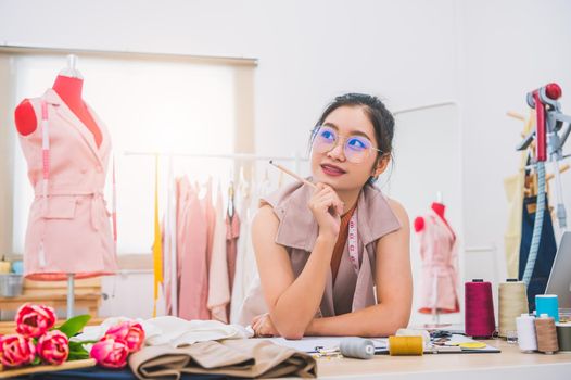 Attractive Asian female fashion designer working in home office workshop. Stylish fashionista woman creating new cloth design collection. Tailor and sewing. People lifestyle and occupation concept