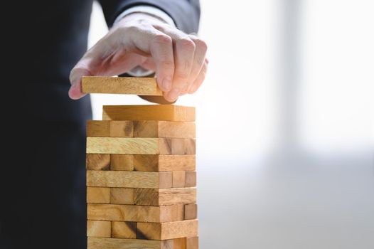 Businessman arranging wood block and stacking as tower by hand. Business organization and company growth progress. Success of strategy and money investment concept. Risk management project theme