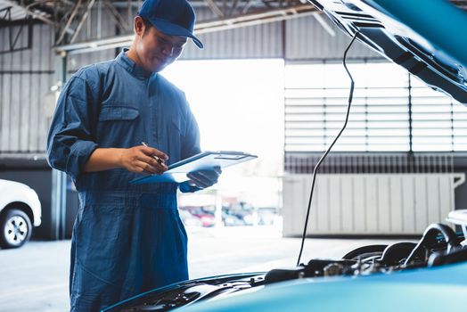 Car mechanic holding clipboard and checking to maintenance vehicle by customer claim order in auto repair shop garage. Engine repair service. People occupation and business job. Automobile technician