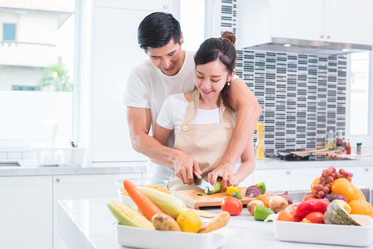 Asian lovers or couple cooking and slicing vegetable in kitchen room. Man and woman looking each other in home. Holiday and Honeymoon concept. Valentine day and wedding theme