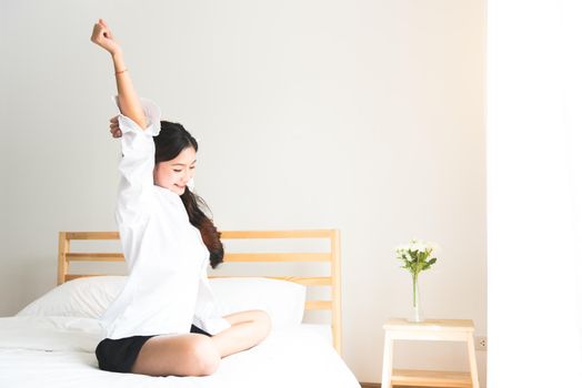 Rear view of woman stretching in morning after waking up on bed near window. Holiday and Relax concept. Lazy day and Working day concept. Office woman and worker in daily life theme