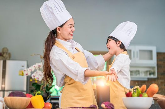 Happy beautiful Asian woman dress up cute little boy chef outfit for prepare to cooking in home kitchen. People lifestyles and Family. Homemade food and ingredients concept. Two Thai people life