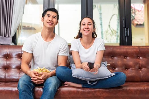 Asian couples watching television together on sofa in their home. People and lifestyles concept. Vacation and holiday concept. Honeymoon and pre wedding theme. Happy family activity in valentines day