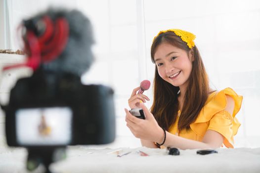 Happy Asian young beauty blogger girl training how to be make up artist in home studio. Woman speaking in front of camera as vlogger. Female vlog blogger recording video tutorial upload to Internet