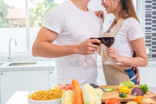 Closeup of drinking wine on happy Asian young married couple hands in home kitchen. Boyfriend and girlfriend cooking together. People lifestyle and romantic relationship concept. Valentines day