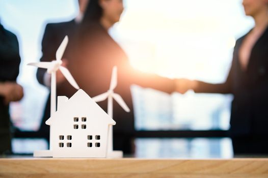 Closeup of home and windmill props with business people doing handshake after contract agreement successfully. House and wind turbine green energy concept. Clean power for future industrial technology