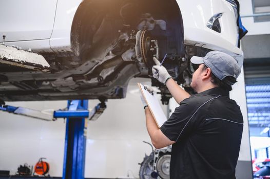 Asian male car technician car maintenance for customers according to specified vehicle maintenance checklist. Disk brake pad wear automotive repairing on vehicle. Safety inspection check service