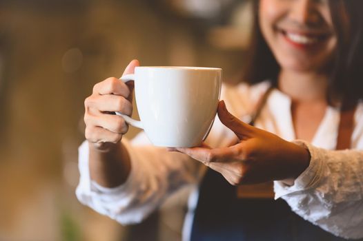 Closeup of white coffee cup with beautiful Asian woman barista background for serving to customer. Job and occupation. Food and drink beverage. Coffee shop and Cafe. Business and restaurant ownership