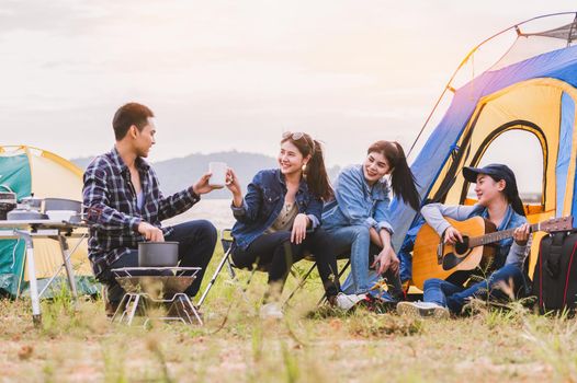Group of Asian friendship clinking drinking bottle glass for celebrating in private party with mountain and lake view background. People lifestyle travel on vacation concept. Picnic and camping tent