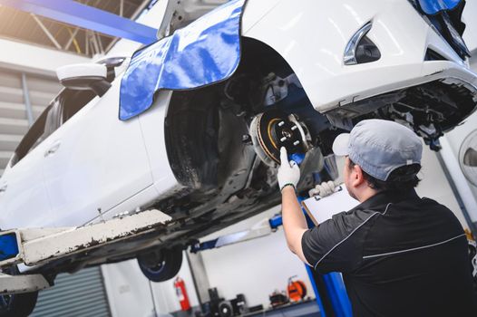 Asian male car technician car maintenance for customers according to specified vehicle maintenance checklist. Disk brake pad wear automotive repairing on vehicle. Safety inspection check service