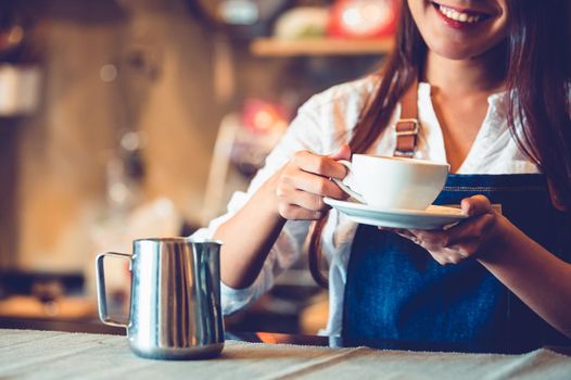 Closeup of professional female barista hand making and holding white cup of coffee. Happy young woman at counter bar in restaurant background. People lifestyles and Business occupation concept