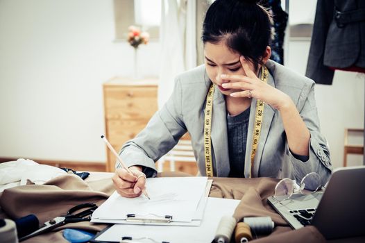 Business Asian fashion designer have no idea when designing new collection of dress in workshop studio. Dressmaker headache and negative thinking concept. Tailor woman stressed writing zigzag stroke