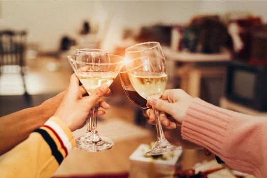 Hands of people celebrating New year party in home with wine drinking glasses and present background. New year and Christmas party concept. Happiness and Friendship and Funny together. Clinking glass 