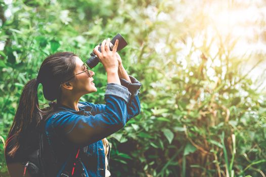 Beautiful Asian woman with binoculars telescope in forest looking destination. People lifestyles and leisure activity. Nature and backpacker traveling jungle background. Bird watching and living