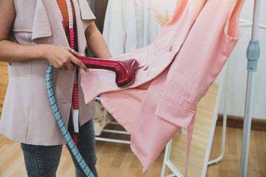 Woman using steaming iron to ironing fashion shirt in laundry room. Girl doing stream vapor iron for press clothes in hand. Launder concentrate work and delivery to customer. Part time job occupation
