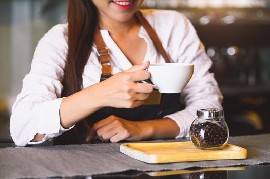 Closeup of white coffee cup with beautiful Asian woman barista background for serving to customer. Job and occupation. Food and drink beverage. Coffee shop and Cafe. Business and restaurant ownership