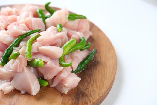 raw chicken slice and green chili on a chopping board on table .