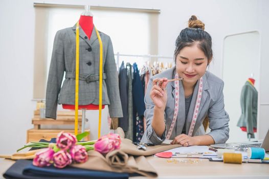 Attractive Asian female fashion designer  working in home office workshop. Stylish fashionista woman creating new cloth design collection. Tailoring and sewing. People lifestyle and occupation concept