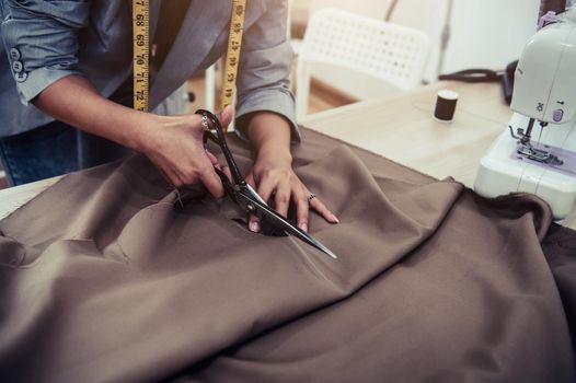 Dressmaker cutting dress fabric on sketch line with sewing machine. Fashion designer tailor or sewer in workshop studio designing new collection clothes. Business owner shop and entrepreneur concept